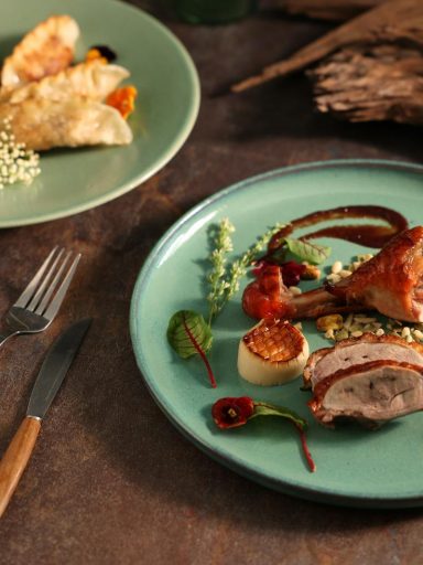 Delicious gourmet goose leg and dumplings plated artistically in a fine dining setting.