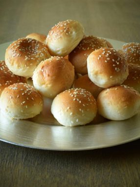 A stack of freshly baked sesame bread buns displayed on a silver plate, ready for breakfast or a snack.