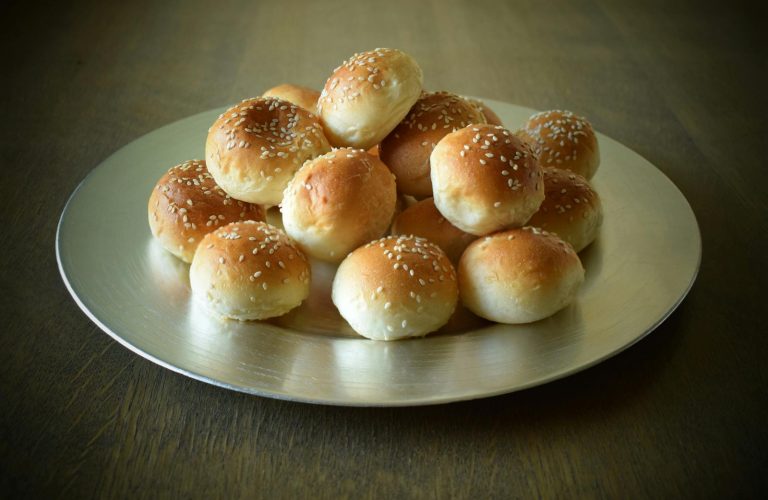 A stack of freshly baked sesame bread buns displayed on a silver plate, ready for breakfast or a snack.