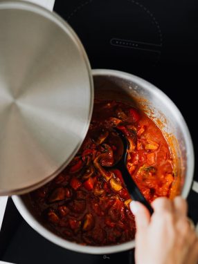 Close-up of shakshuka cooking in pot with spoon stirring. Perfect for culinary enthusiasts.