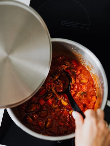 Close-up of shakshuka cooking in pot with spoon stirring. Perfect for culinary enthusiasts.