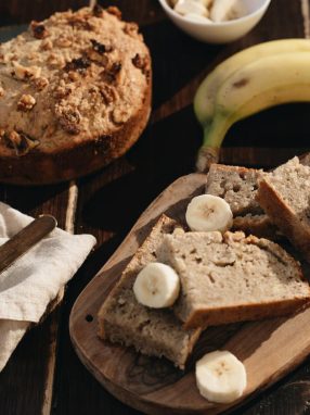 A rustic presentation of homemade banana bread with fresh bananas on a wooden board.