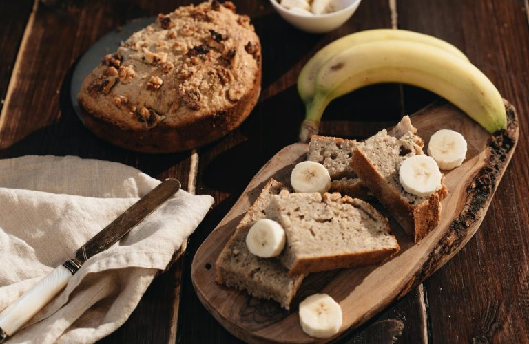A rustic presentation of homemade banana bread with fresh bananas on a wooden board.
