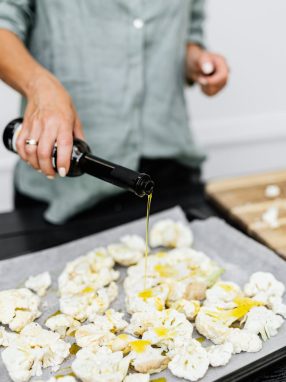 Close-up of a woman preparing a healthy keto meal by pouring olive oil on cauliflower florets.