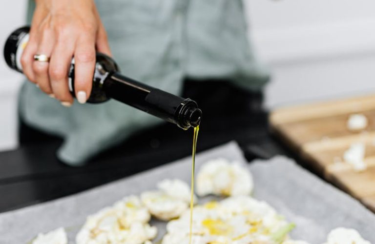 Close-up of a woman preparing a healthy keto meal by pouring olive oil on cauliflower florets.