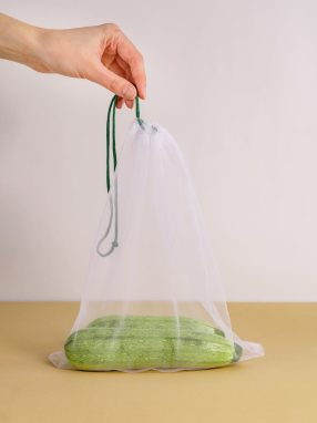 A hand holding a mesh bag containing zucchinis, highlighting sustainable packaging solutions.