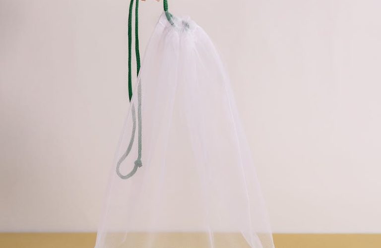 A hand holding a mesh bag containing zucchinis, highlighting sustainable packaging solutions.